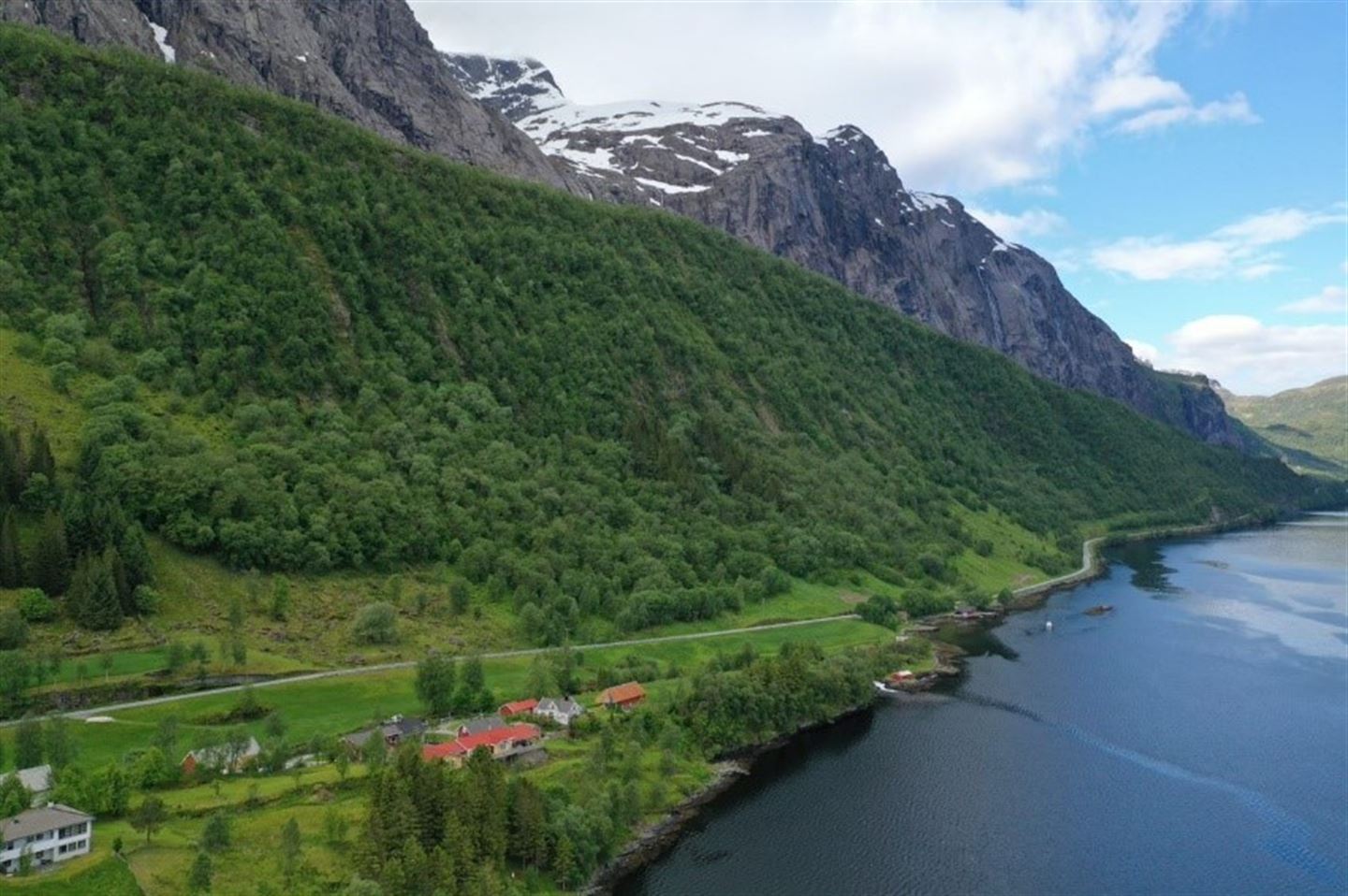 Fjord med grønn skog og steile fjellsider lengre bak. Nokre hus nede ved fjorden.