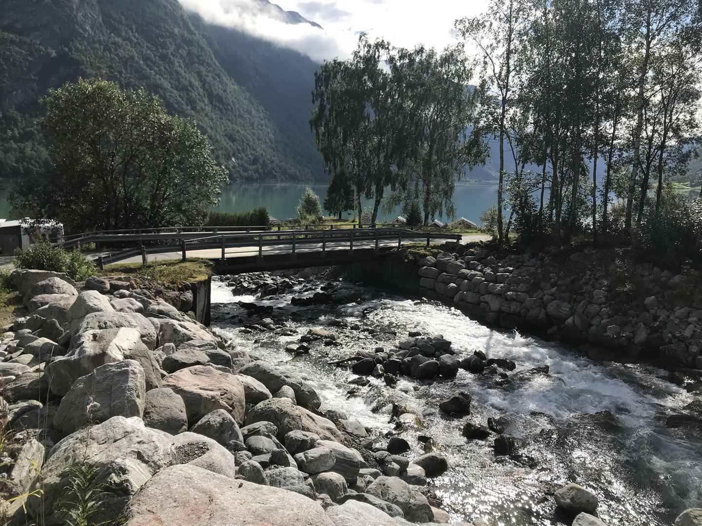 Veg med bru som kryssar elv, eit vatn i bakgrunnen.