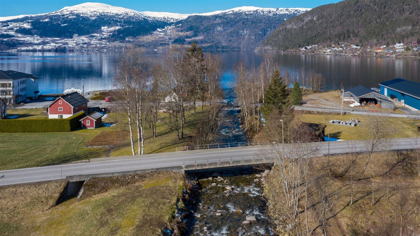 Bilde tatt frå lufta, skrått overfor Storelva bru i Innvik i Stryn. Vegen og brua går midt i bildet, med elva flytande under som renner ut i fjorden. I bakgrunnen er det snødekte fjell. 