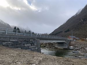 Bru i betong som kryssar elv. Grå himmel og seinhaust.