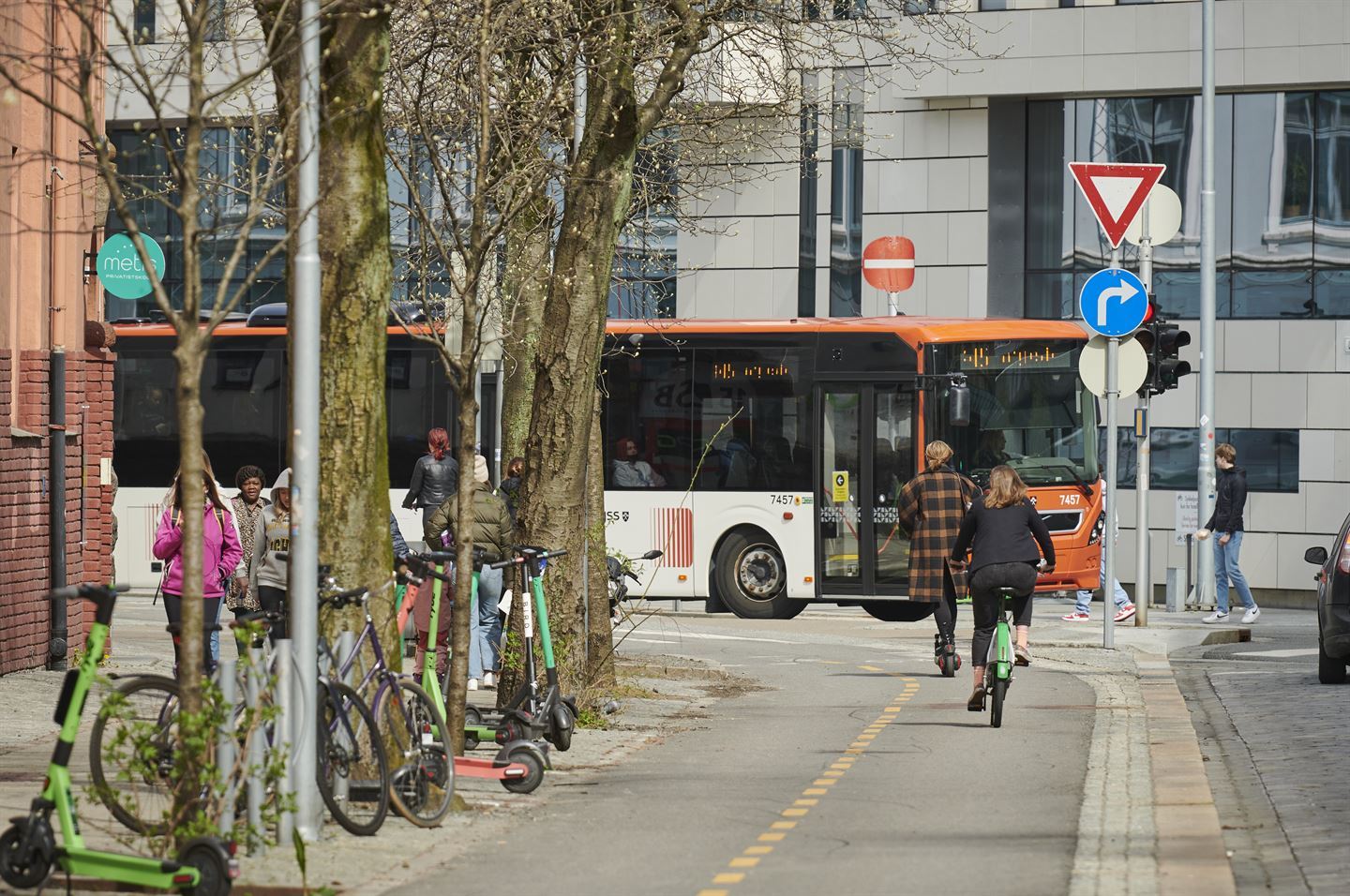 Bytrafikk, syklistar på sykkelveg og buss i bakgrunnen. Elsparkesyklar står på fortauet, vår.