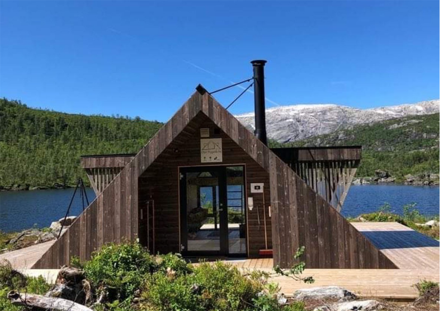 Dagsturhytta i modalen, Olav Nygard Bu med blå himmel og snøfylte topper i bakgrunnen. 