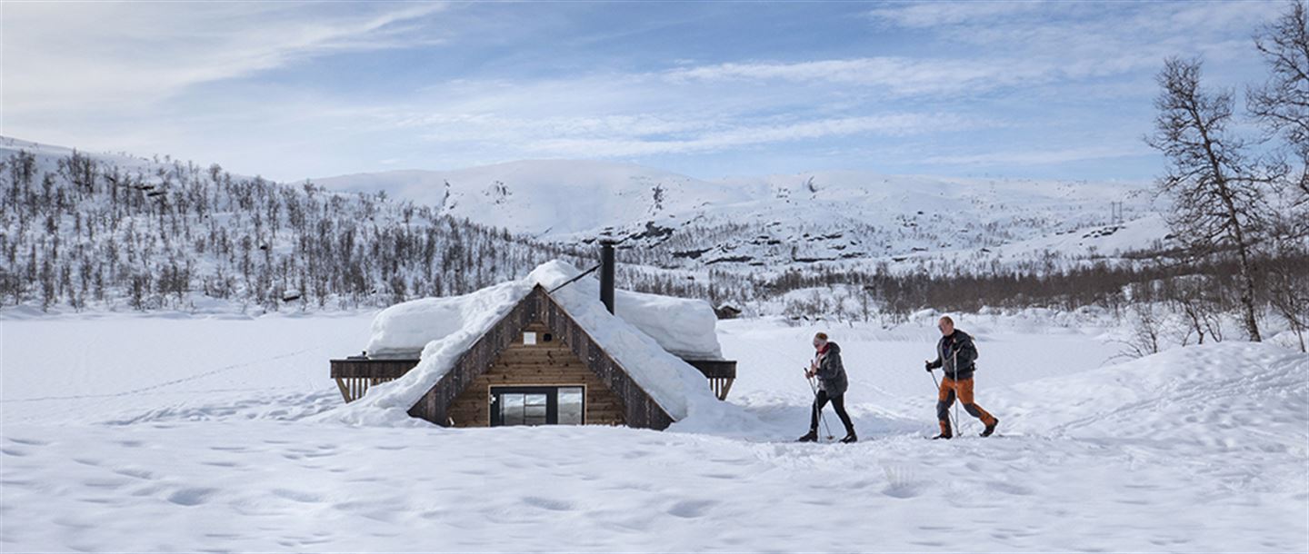 To menneske på langrennski ved dagsturhytta Olav Nygards bu i Modalen. Berre halve hytta er synleg over snøen.