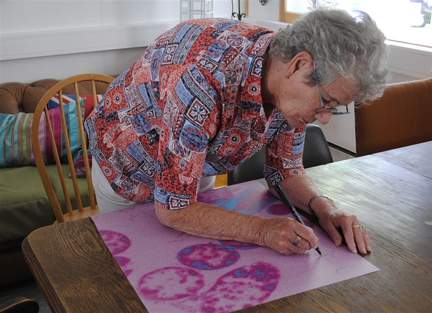Foto som syner ei eldre kvinne som skriv stadnamn på Fyllingsdalen oppå eit kunstverk der ein bakterie er forstørra opp. 