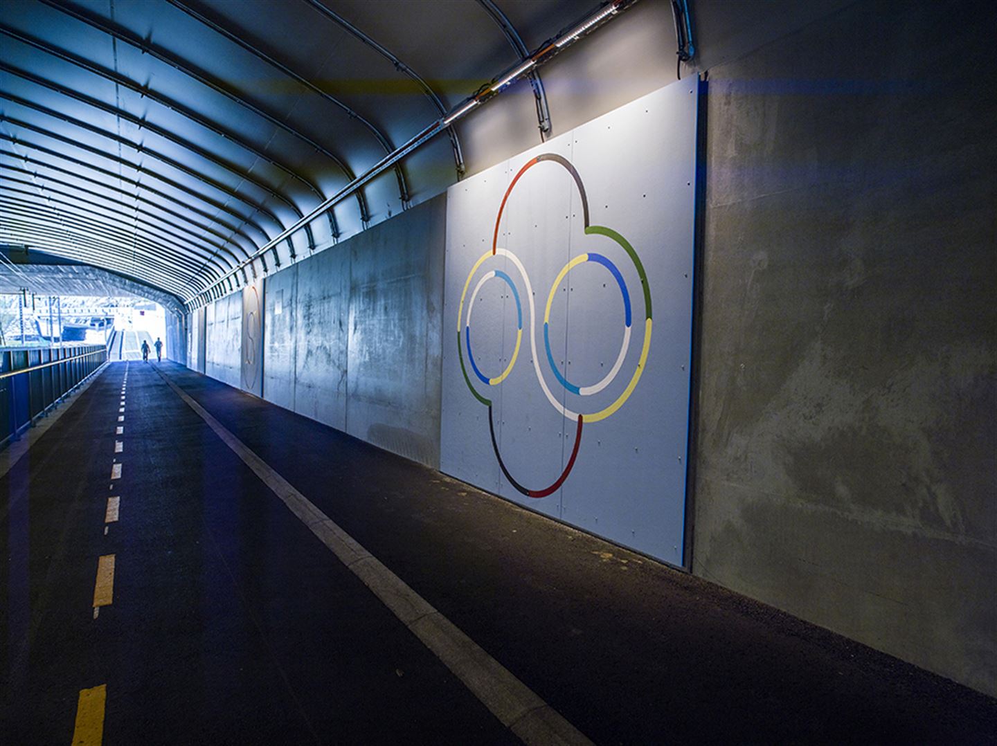 Foto av kunstverket Sirkelspill inni ein bybanetunnel. Det er fargerike figurar målt på betong.
