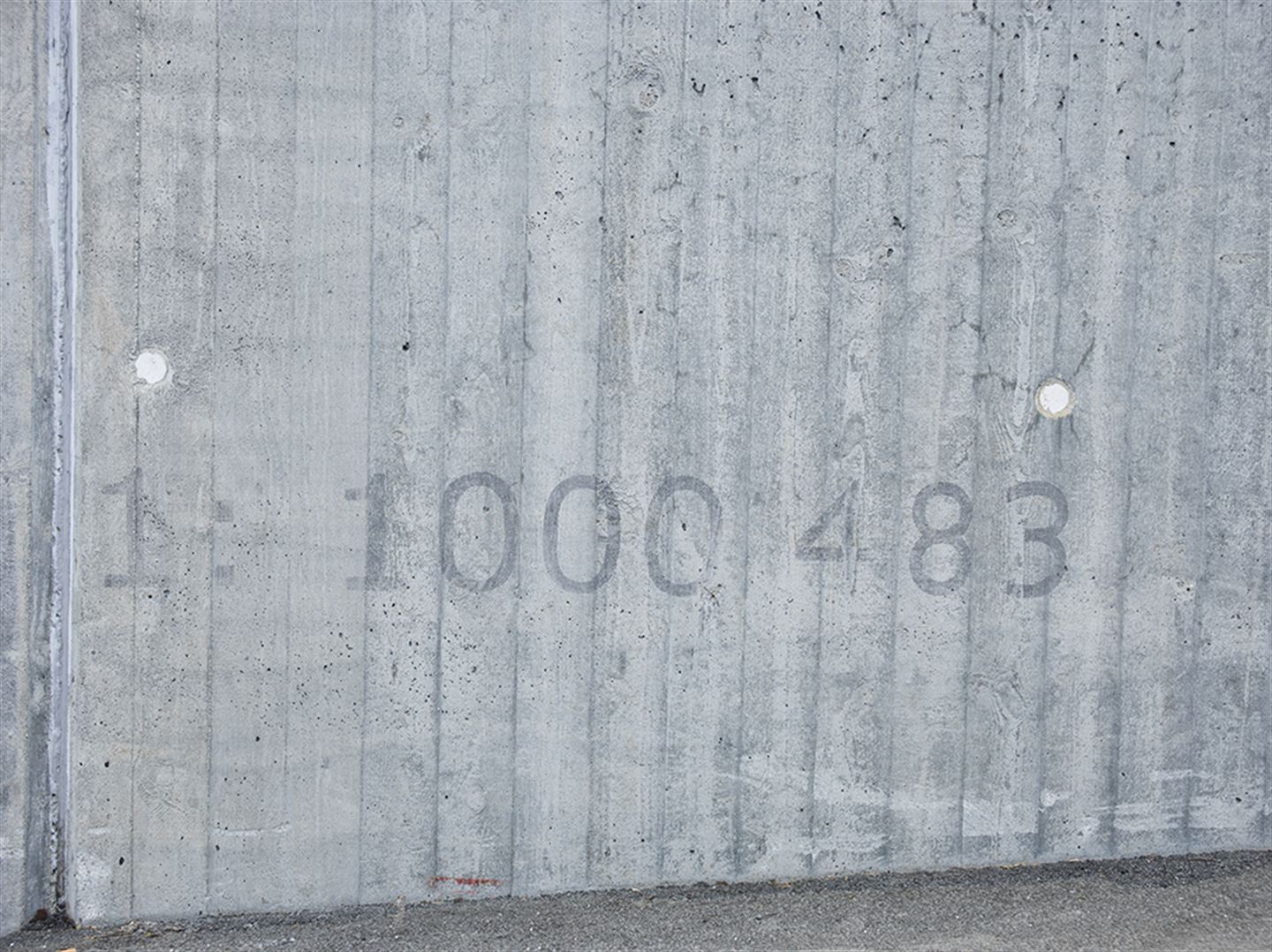 Foto av kunstverket 1: 1 000 483 langs bybanetraseen. Kunstverket er målt på betong, og det syner namnet på kunstverket.