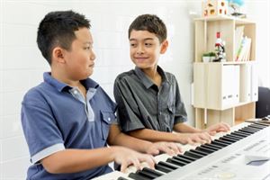 To små gutar som spelar piano med begge hendene.