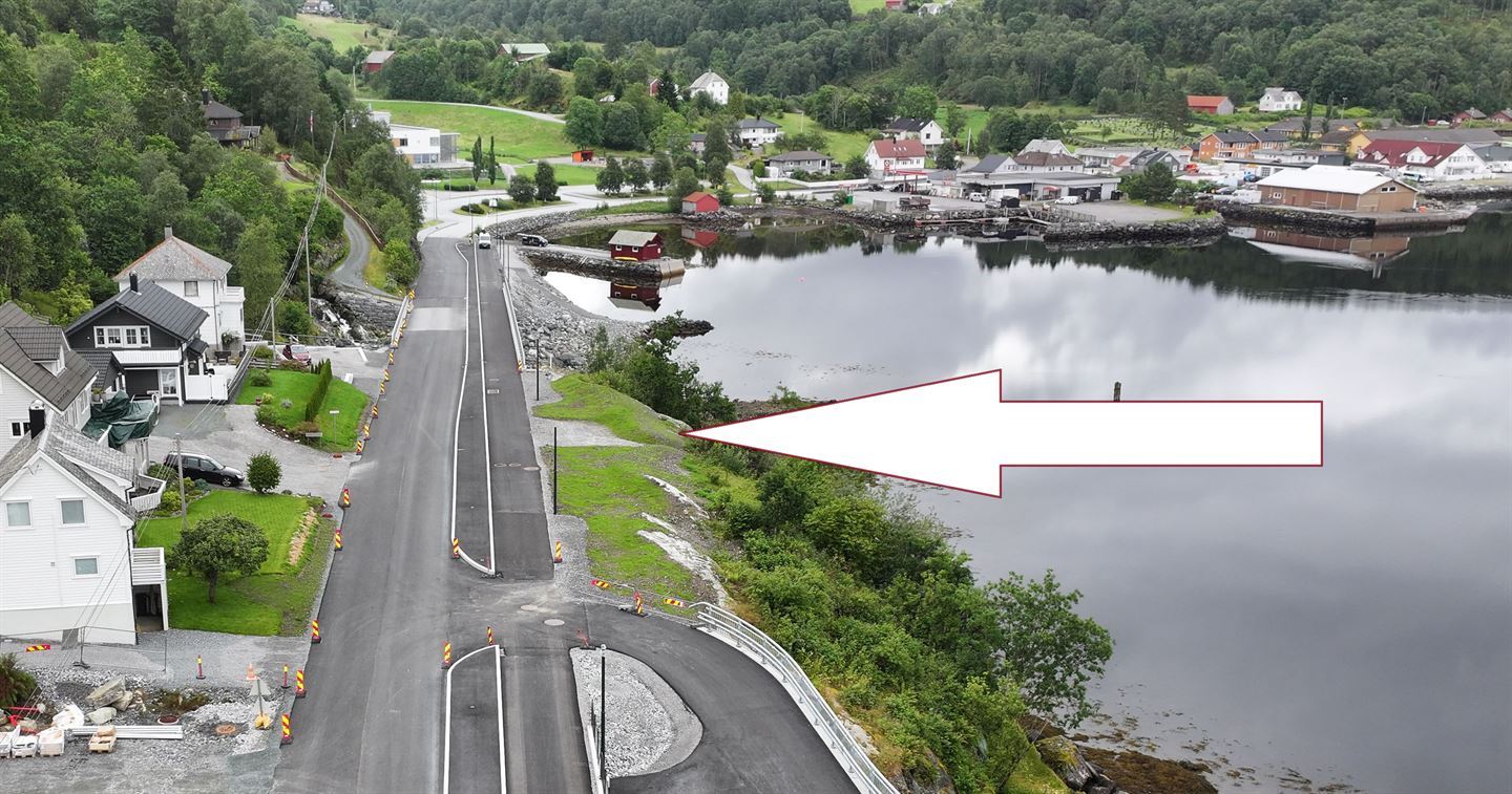 Opningsmarkeringa skal vere rett ved nye indre Hovland bru, ned mot sjøen. Sjå grusa område markert med pil på dette bildet. (Foto: Stian Støfringsstøl/Vestland fylkeskommune)