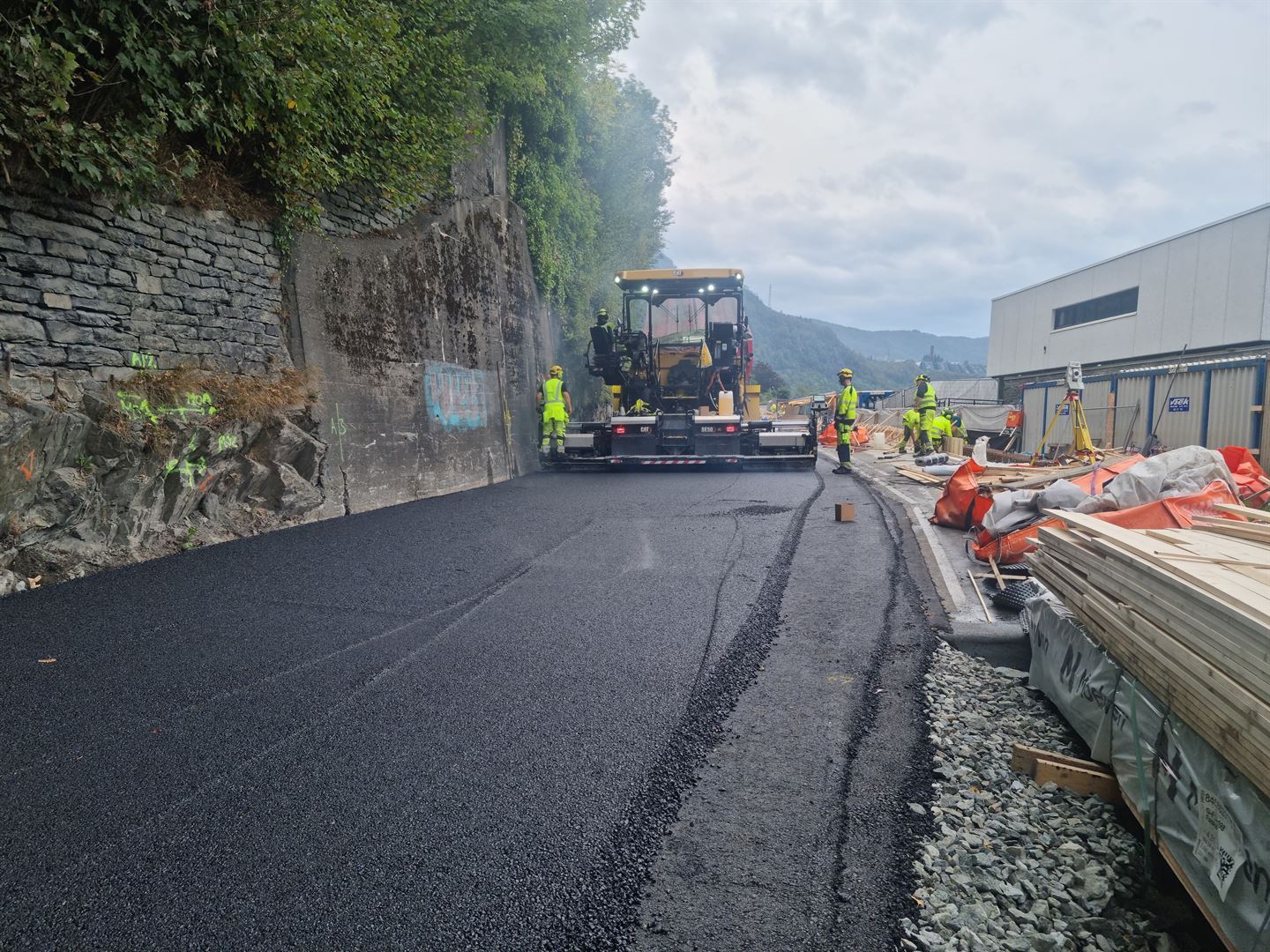 To personar som står på ein veg og på kvar sida av eit køyretøy som blir brukt når ein legg asfalt.
