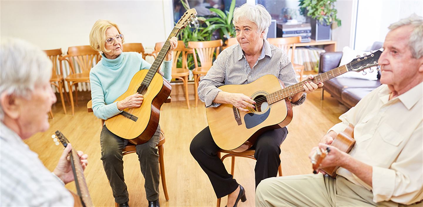 Fire eldre menneske som sit saman og spelar gitar.