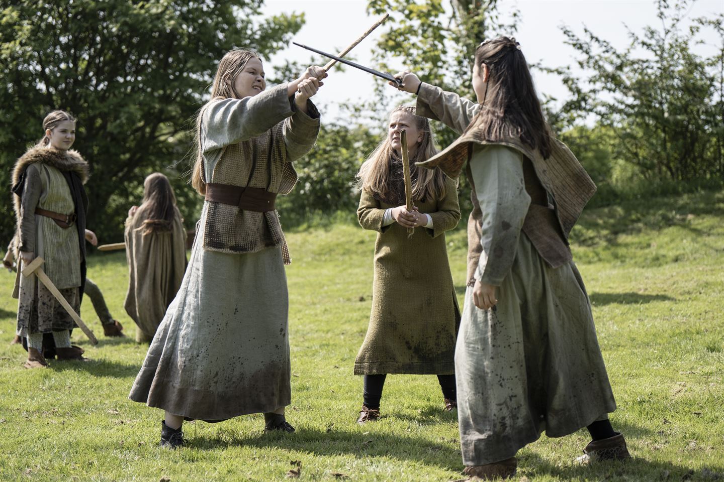 Tre jenter forkledd som vikinger sloss med tresverd.